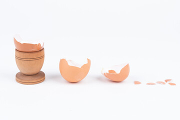 Horizontal shot of broken egg shell in old wooden egg stand and multiple other broken shells on a white surface. Minimalism. Conceptual art for food or animal products. Sustainability issue. - Powered by Adobe