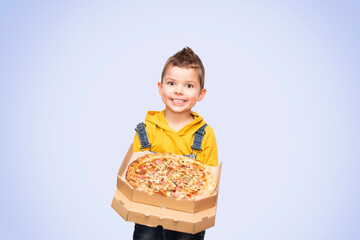 Little cute baby boy in a yellow sweater and denim overalls smiles and holds an open box with pizza isolated on background.