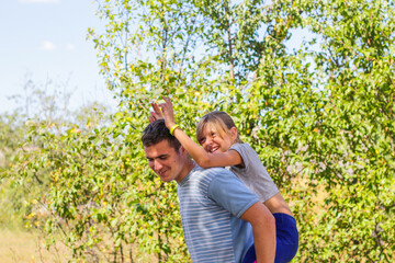 Defocused brother giving sister ride on back. Portrait of happy girl with funny horns on man shoulders, piggyback. Family playing outside. Summer holidays smiling people concept. Out of focus