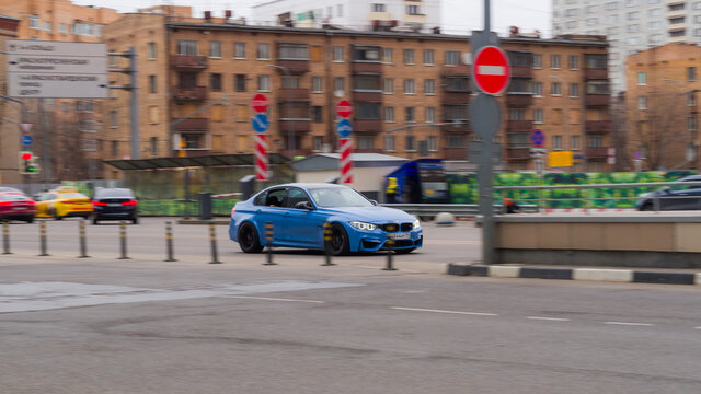 blue sport car BMW M3 with black wheels riding next to the old buildings.