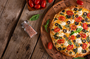 In the right corner of the photo we see a pizza on a wooden stand. To the left of the pizza are spices in a glass bottle, and in the background we see tomatoes. Wooden table. Country style.