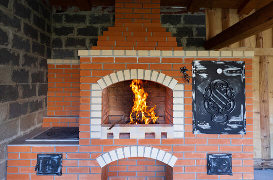 The fire is lit in a summer brick oven for barbecue, grill and other outdoor dishes. Outdoor Summer Kitchen With Pizza Oven And Barbeque Grill. Outdoor Brick BBQ Grill And Baking Oven.