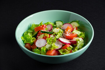 Fresh vegetable salad in a ceramic bowl on gray background. Seasonal summer dish of tomatoes, cucumbers and radishes.