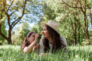 Girl gives her mother flowers to smell lying in grass in summer park. Family having fun outdoors...