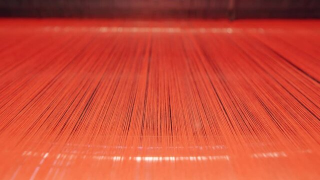 Red threads are moving through a weaving machine at high speed