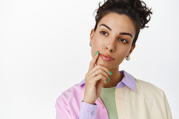 Thoughtful brunette girl making choice, looking at logo with ponder, touch face and thinking, standing against white background