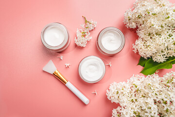 Set of natural cosmetics for face care, white cream with lilac flowers on pink background, top view