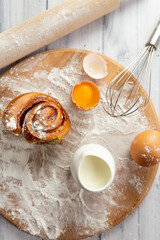 The ingredients for making baked goods on the table are wheat flour, eggs, milk, as well as a rolling pin and a wooden board. top view