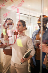 Happy creative colleagues writing on glass wall while working on new business project in the office.