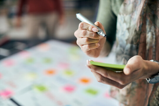 Close-up of female entrepreneur writing on adhesive note while working in the office.