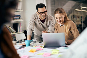 Young happy freelancers cooperating while working on laptop in the office.