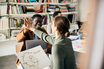 Happy creative coworkers giving high-five while working on new business project in the office.