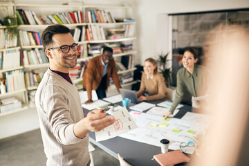 Happy freelancer presenting to his colleagues new business plans on meeting in the office.