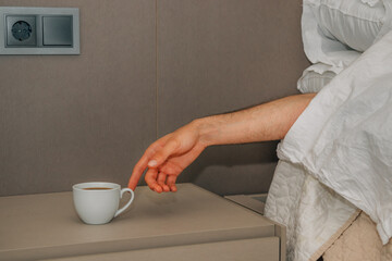 Fototapeta na wymiar hand on the bed looking for the cup of coffee to wake up