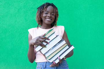 A young beautiful African-American woman on a green background with books in her hands. Human emotions