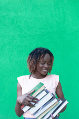 A young beautiful African-American woman on a green background with books in her hands. Human emotions