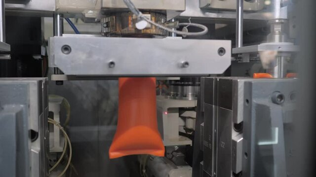 Automatic blow molding machine - manufacturing of empty orange plastic jerrycans at factory, exhibition - close up. Industry, packaging, automated technology equipment concept