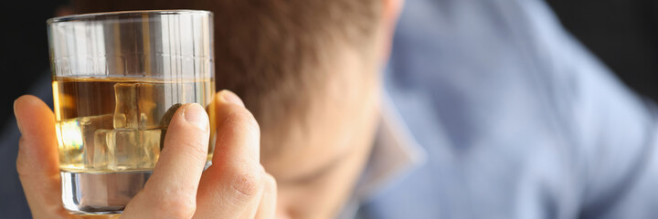Sad man holding glass of whiskey and ice in his hands closeup