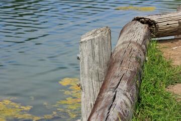 Posts at Sterling Lake on the Island to hold up the dirt with green grass and blue water with moss in Sterling Kansas USA.