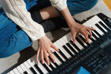 Girl sitting on the floor and playing piano. Close-up view.