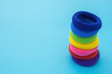 Column of multicolored scrunchies, elastic hair ties, cotton hair ponytail holders, seamless hair bands on blue backdrop