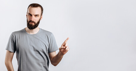 Portrait of cheerful young handsome man smiling looking at camera pointing finger upwards on white background with space for advertising mock up