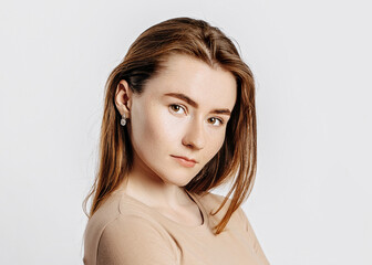 Beautiful young girl smiling and posing looking at the camera on a white isolated background. Positive brunette woman in a beige jumper. Kind look.