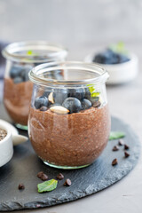 Chocolate chia pudding with blueberry, almonds and mint on top in a glass jar on a gray concrete background. Healthy food. Copy space.