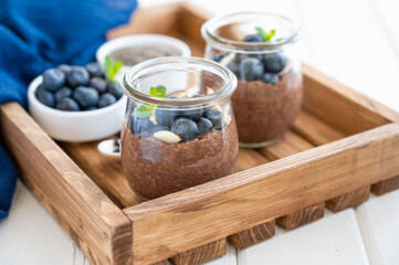 Chocolate chia pudding with blueberry, almonds and mint on top in a glass jar on a white wooden background. Healthy food. Copy space.