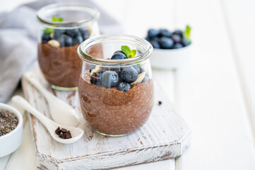 Chocolate chia pudding with blueberry, almonds and mint on top in a glass jar on a white wooden...