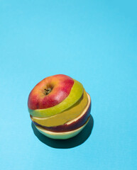 Organic apple slices in red, green and yellow stacked on each other against sky blue sun lit background. Minimal summer fruit composition.