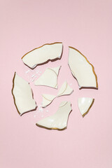 Broken wedding plate in circle shape in ivory color with gold edges against pastel pink background....