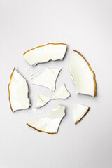 Broken wedding plate in circle shape in ivory color with gold edges against light gray background. Minimal creative party concept.