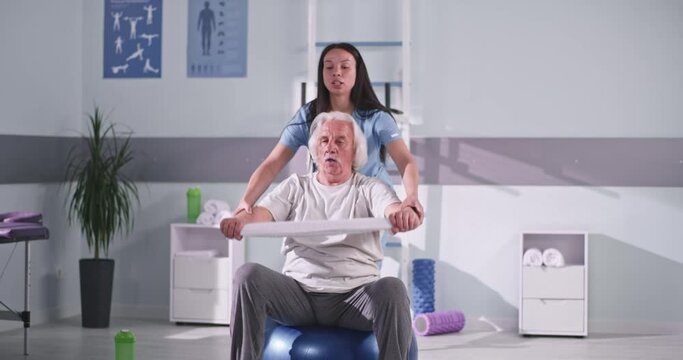 Rehabilitation therapist helping senior patient to exercise with towel