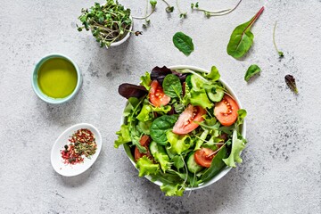 Fresh salad with fresh vegetables, ripe tomatoes, cucumber, lettuce and microgreen  in a bowl on a gray background. Healthy raw food concept.