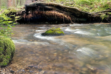 A slow shutter speed photo of a cascading river flowing around a rock with bright green moss.