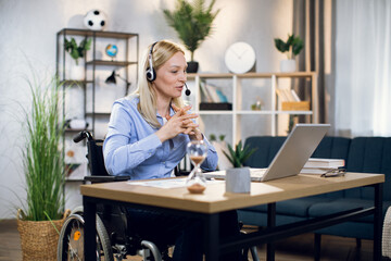 Charming woman with special needs talking and gesturing during video conference on modern laptop. Young blonde working remotely while staying at home.