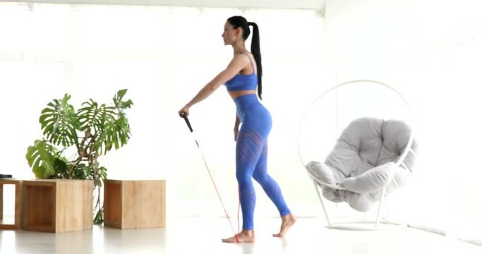 A sporty woman is doing exercises on quarantine. The woman is getting fit and using a fitness band to strengthen her muscles.