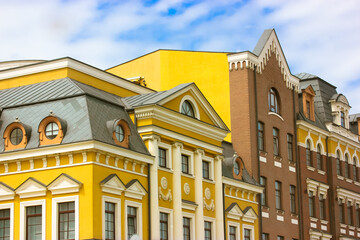 Classical architecture exterior. Beautiful bright yellow and brown buildings front view against a blue cloudy sky. Colorful houses with round and square windows, white columns. Picturesque cityscape.