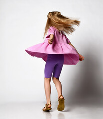 blonde preschool girl, in a summer outfit and sandals, spinning on a light studio background.