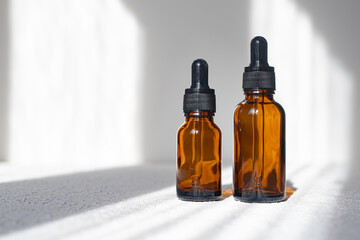 Glass bottle of mineral beauty oil with dropper for skin, hair. Product packaging serum on a white background. Women's cosmetics skin care cream with shadows.