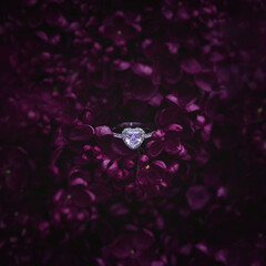 White gold engagement ring with a heart-shaped diamond lying among  dark purple lilac flowers. An...