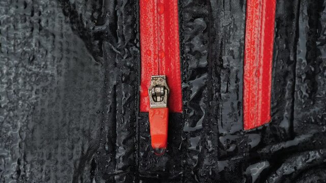 Water droplets on the waterproof fabric. Close-up of a waterproof jacket. Black clothes with red zipper