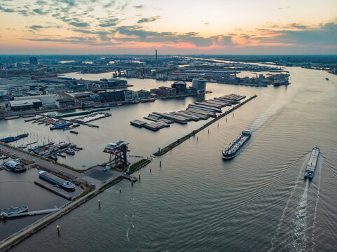 Aerial view of city harbour with boats docked at sunset along Buiten IJ canal in Amsterdam, North Holland, Netherlands.