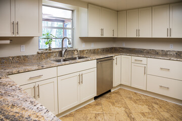 A Modern U-Shaped Kitchen with White Cabinets, Granite Countertops and a Touchless Faucet with Double Bowl Stainless Steel Sink in Front of a Window.
