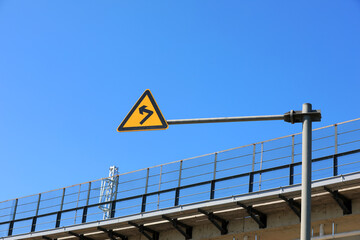 The sign of curve beside the railway bridge is in the background of blue sky