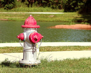 red and silver fire hydrant along the sidewalk next to a neighborhood pond - Powered by Adobe