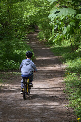 A boy about 8 years old rides a bicycle along a path in the forest in a sports helmet. Back view