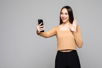 Naklejka premium Beautiful woman with asian appearance taking selfie or speaking on video call using cell phone isolated over gray background