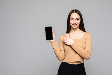Naklejka premium Happy young woman holding blank screen mobile phone over grey background